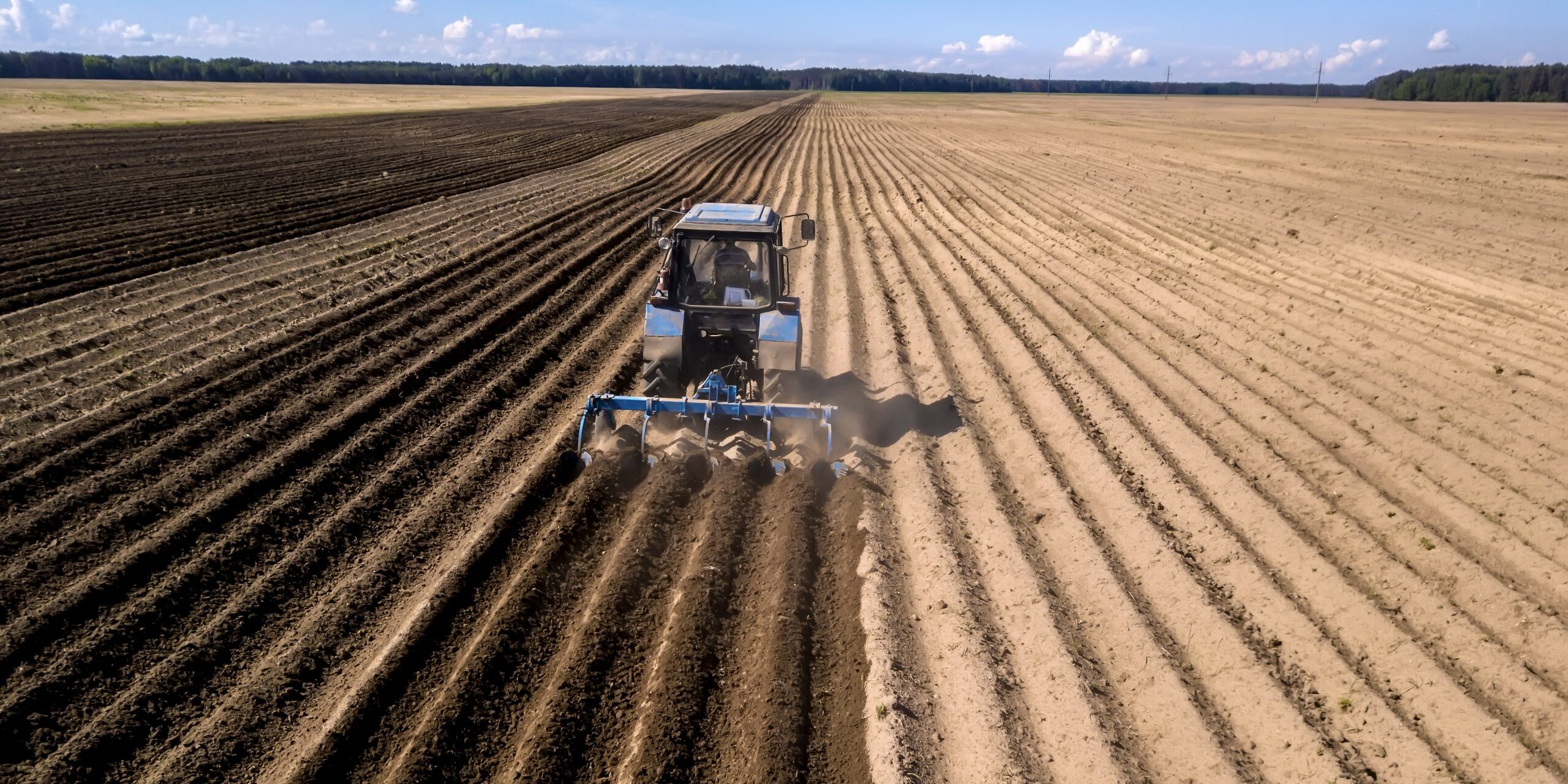 tractor – aerial view of a tractor at work – cultivating a field in spring with blue sky – agricultural machinery