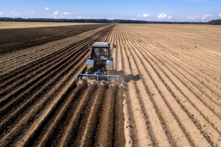 tractor – aerial view of a tractor at work – cultivating a field in spring with blue sky – agricultural machinery